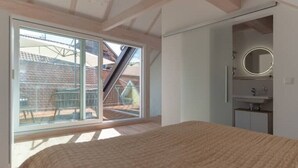 Een slaapkamer met een groot bed, een schuifdeur naar een balkon en een inpandige badkamer met een spiegel en wastafel.