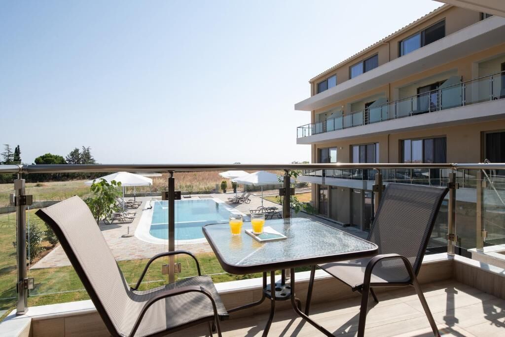 Un balcon avec une table et des chaises en verre, donnant sur une piscine et un immeuble doté de balcons.