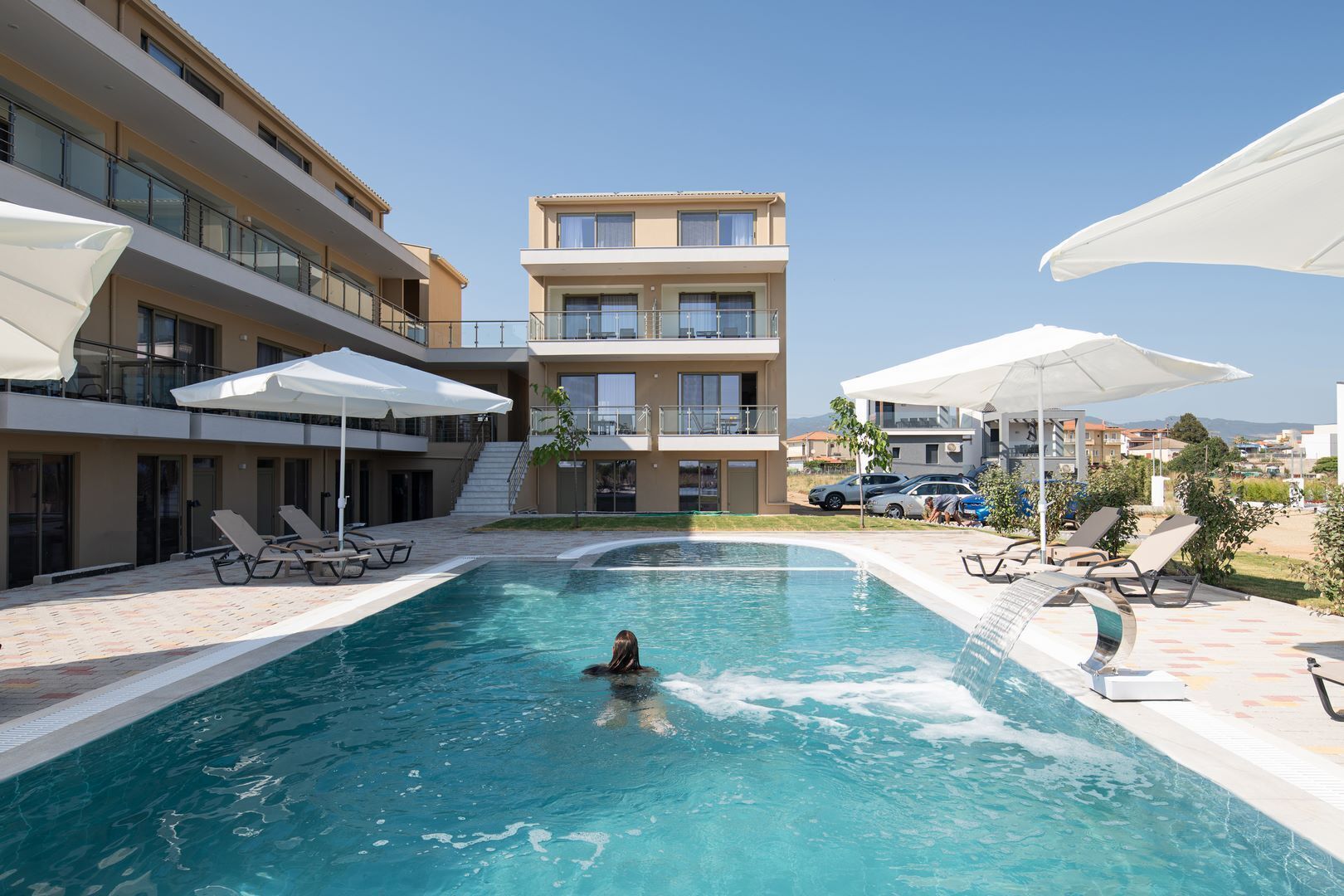 Una piscina con sillas de descanso y sombrillas, rodeada por un edificio de varios pisos con balcones.