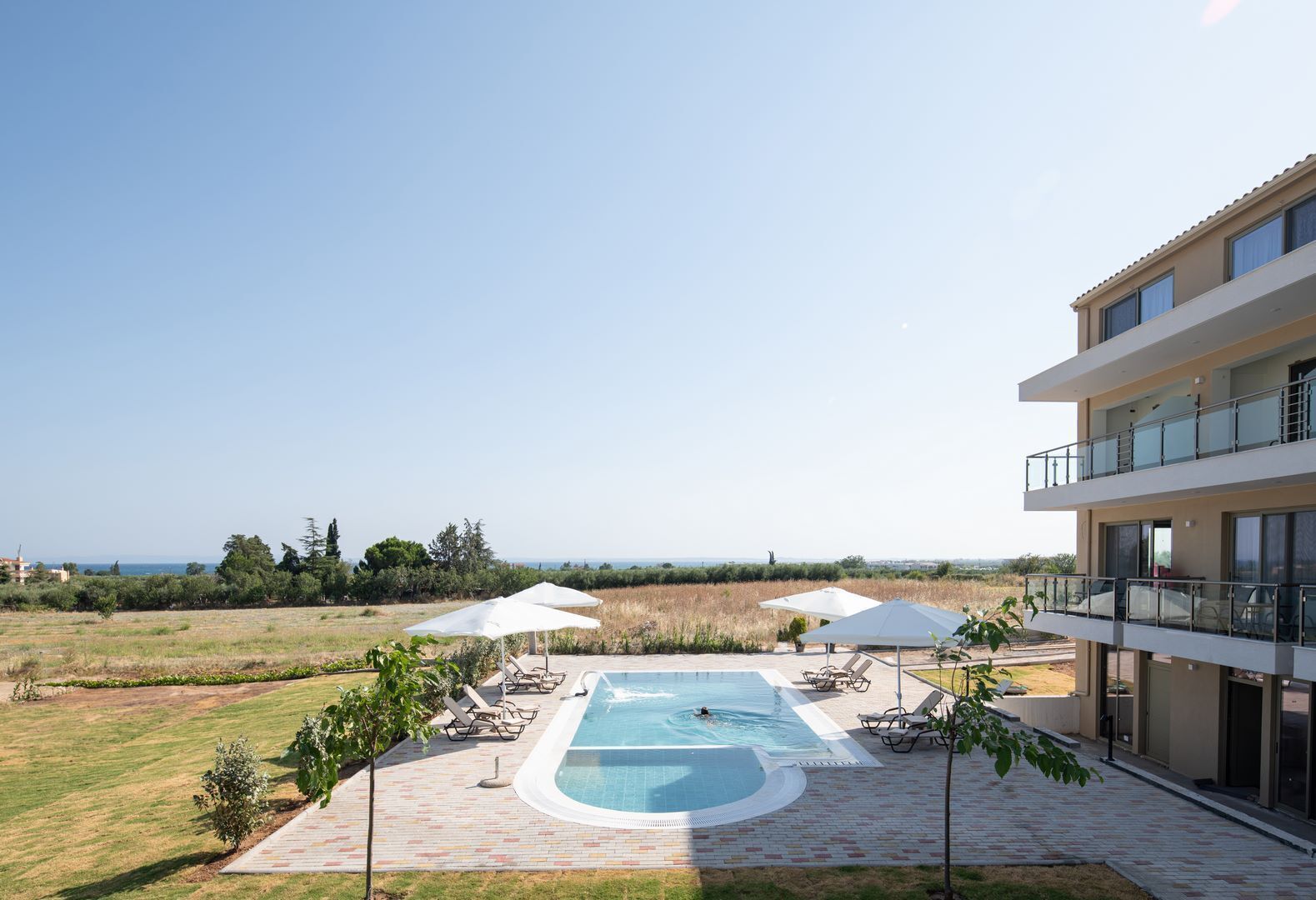 Un espace piscine avec des chaises longues et des parasols, une vue dégagée sur la mer et un bâtiment moderne doté de balcons.