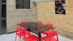 A dining area with a glass table surrounded by red chairs, a brick wall, and a window with a metal frame.