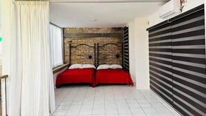 A bedroom with two beds, a brick wall, a window with curtains, and a sliding door.