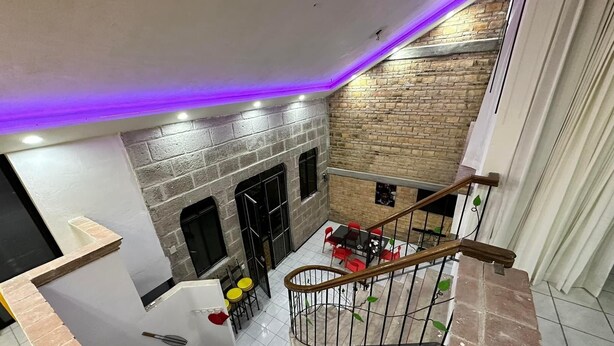 A multi-level interior with a staircase, a dining area with red chairs, and a brick wall.
