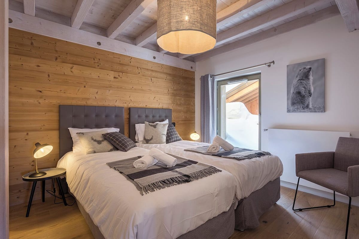 Et moderne soveværelse med træloft, en stor seng med mange puder, et sengebord med en lampe og et vindue med udsigt til det fri.