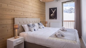 A bedroom with a wooden wall, a bed with white bedding, a mounted picture of a deer, and a window with curtains. - TERRESENS - Le Hameau de Barthélémy (Montvalezan)