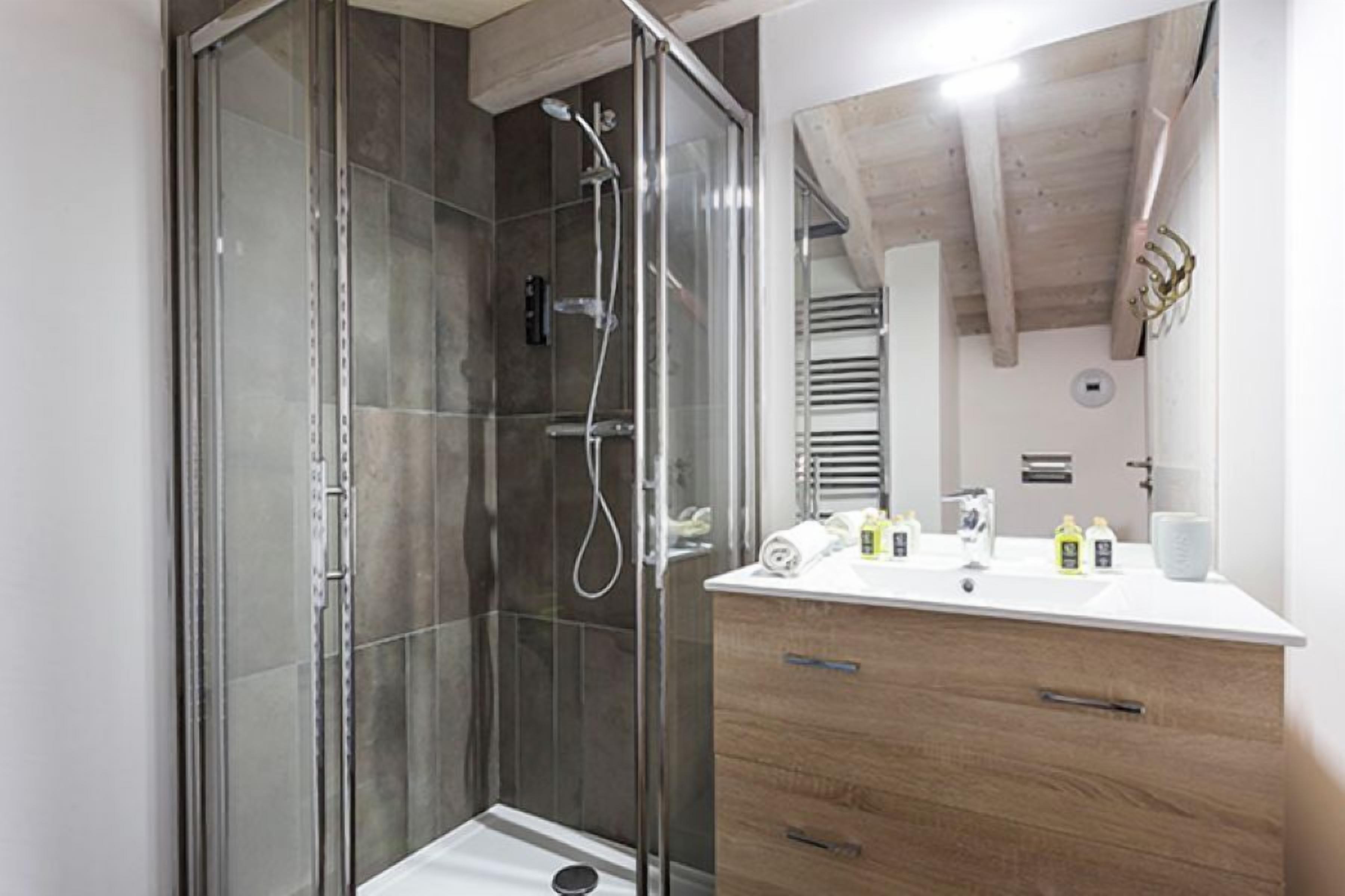 Un baño moderno con ducha envuelta en vidrio, tocador de madera con espejo y encimera blanca.