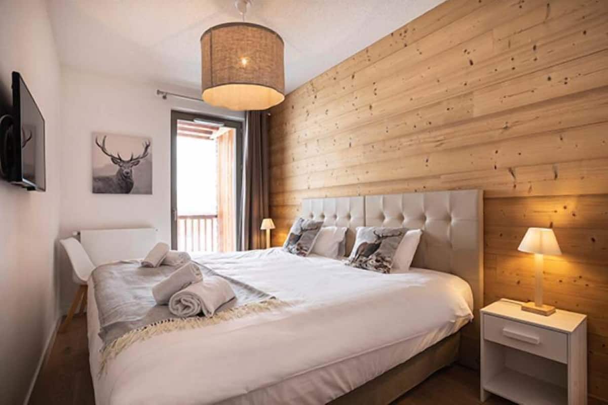 Et soveværelse med en stor seng, et træhovedgærde, et natbord med en lampe og et tv ophængt på væggen.