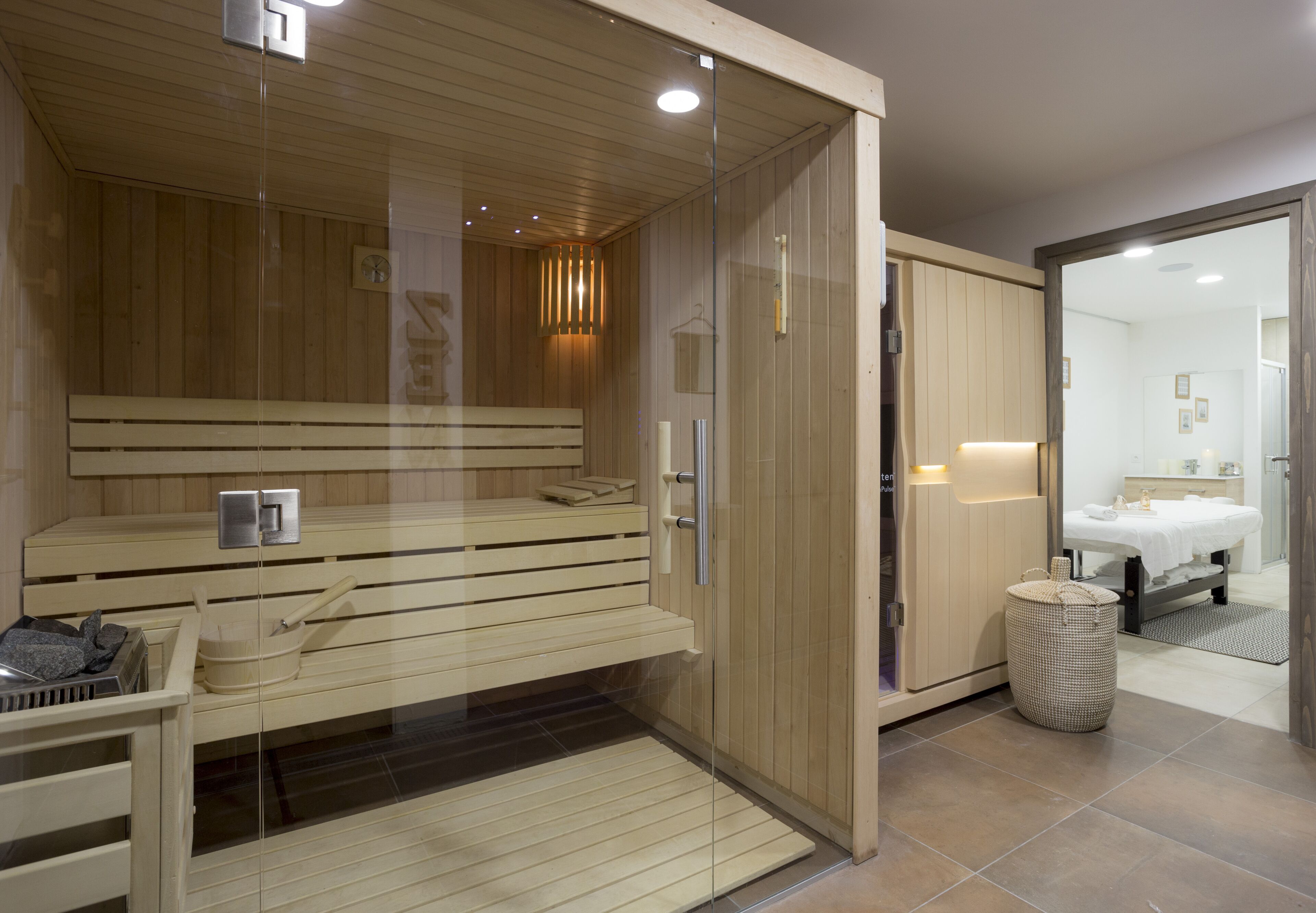 Un sauna moderno con bancos de madera, una puerta de cristal y una pequeña mesa con toallas y un cubo.