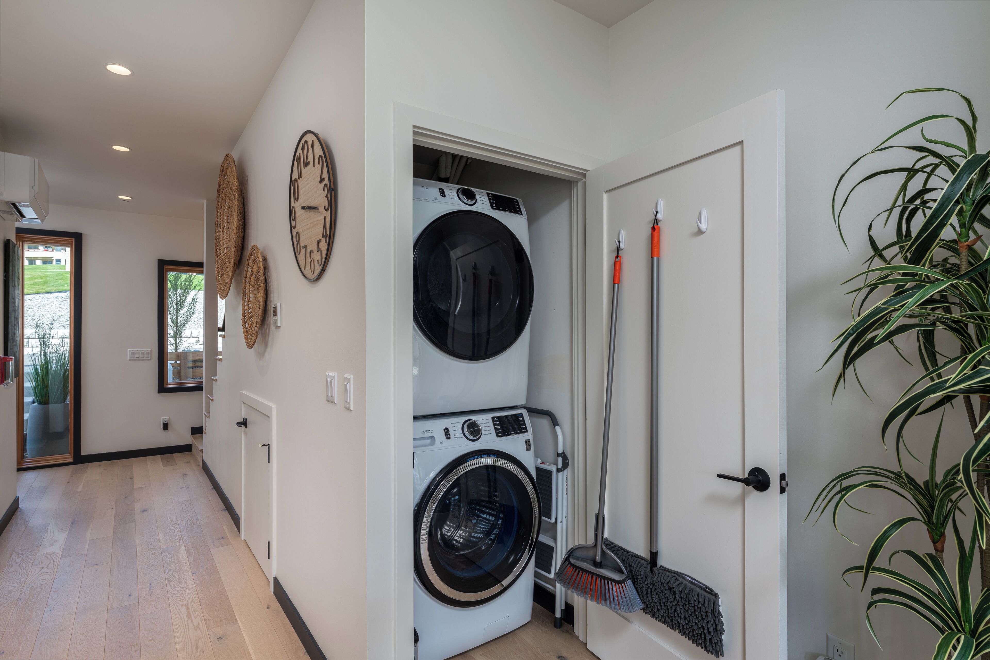 A laundry area with a washing machine and dryer, a broom, and a potted plant.