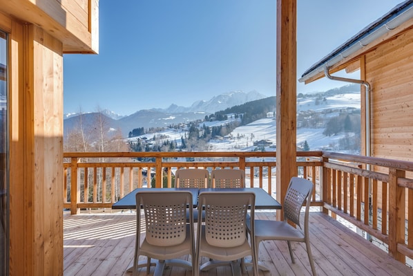 Una terraza de madera con una mesa y sillas, con vistas a un paisaje montañoso nevado.