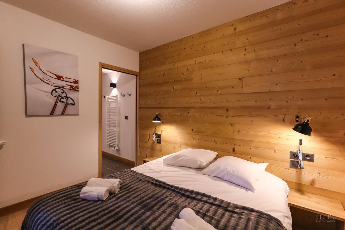 Une chambre à coucher avec une tête de lit en bois, deux lampes de chevet, un lit avec du linge de lit blanc, une couverture à rayures et une serviette sur le lit.