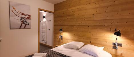 A bedroom with a wooden headboard, two bedside lamps, a bed with white linens, a striped blanket, and a towel on the bed.