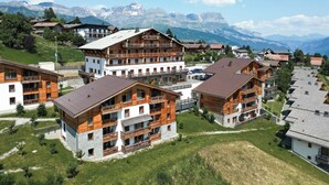 A multi-story hotel with balconies, set against a mountainous backdrop.