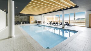 A large indoor swimming pool with clear blue water, surrounded by lounge chairs and a stone wall.