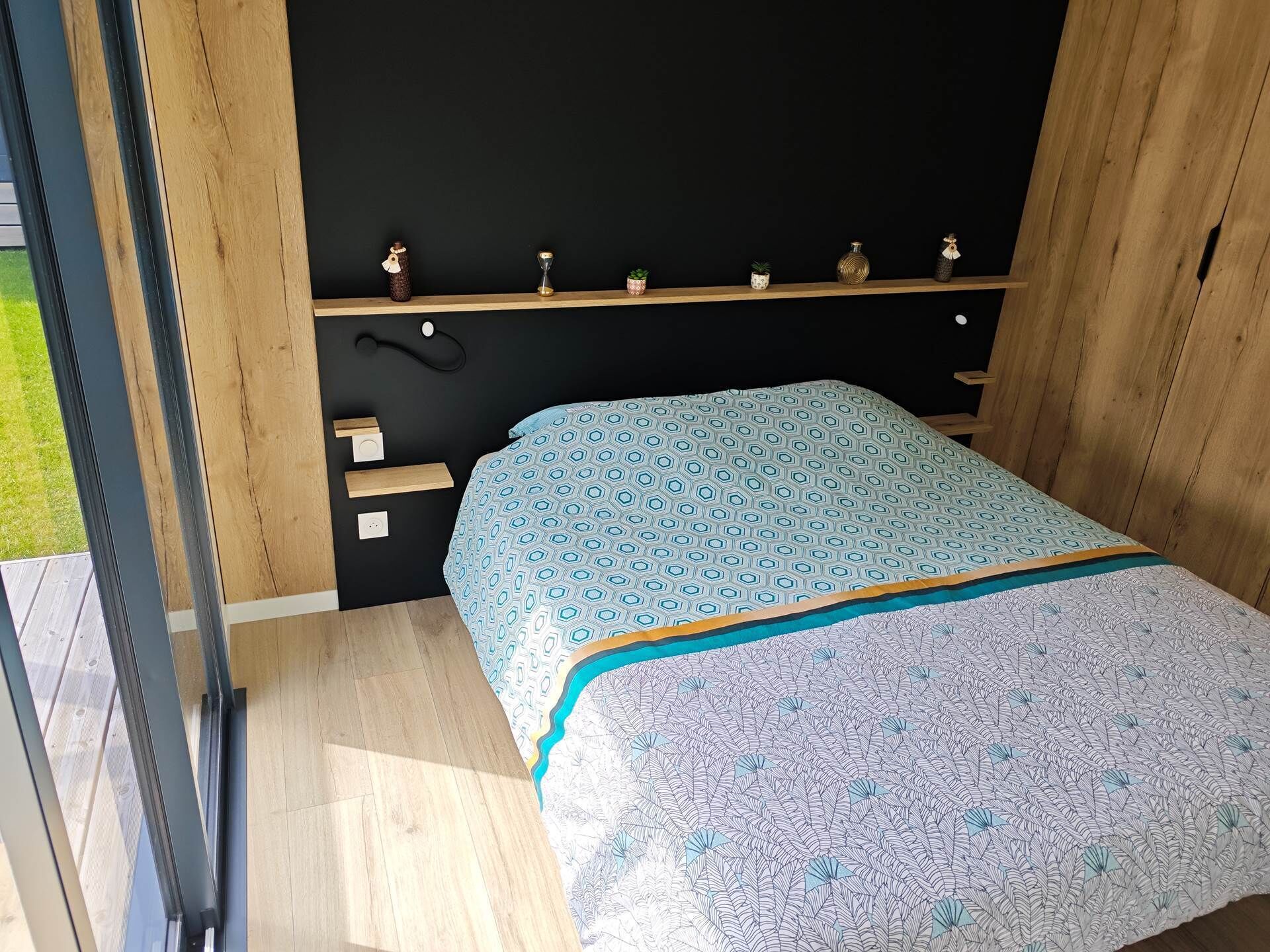 Ein Schlafzimmer mit einem Bett, einem Holzregal mit Dekoration und einem Fenster.