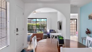 A dining area with a round table, white chairs, and a view of the outdoors through large windows. - Palm Springs Oasis: Gated Condo w/ Pool & Hot Tub (Palm Springs)