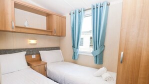 Ein gemütliches Schlafzimmer mit zwei Betten, Holzschränken, einem kleinen Tisch und einem Fenster mit Vorhängen.
