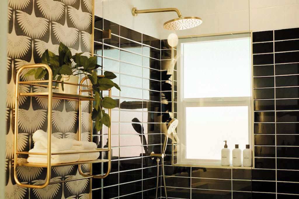 A bathroom with a shower, a window, and a towel rack with plants.
