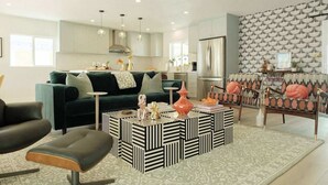 Un soggiorno moderno con divano, tavolino e poltrone, angolo cottura con mobili e una parete decorata.