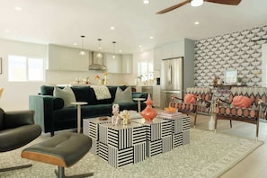 A modern living room with a sofa, coffee table, and chairs, a kitchen area with cabinets, and a patterned wall. - Mod Retreat in Vibrant Palm Springs (Palm Springs)