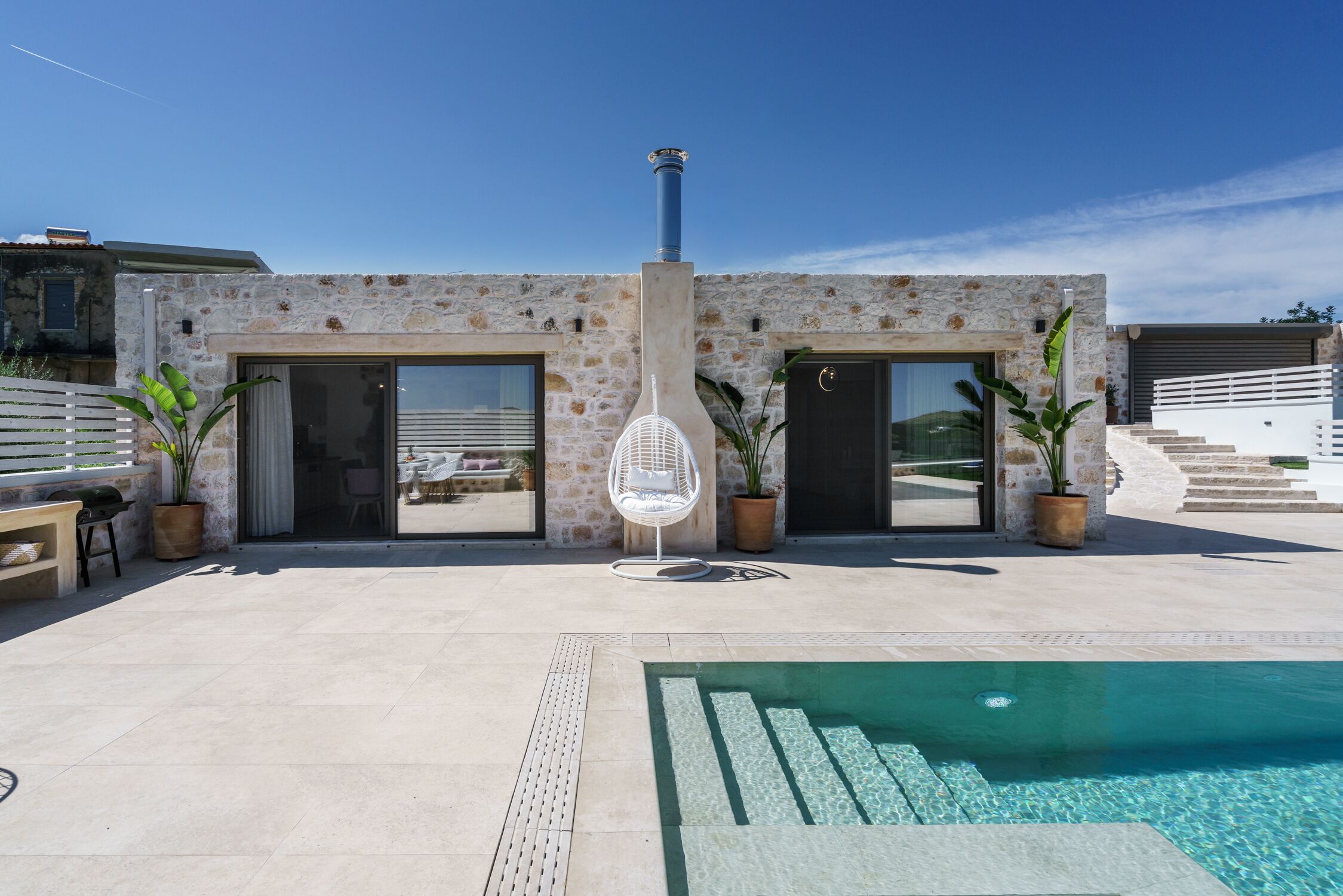 Ein modernes Gebäude mit einer Stein-Fassade, einem Pool und Kübelpflanzen.
