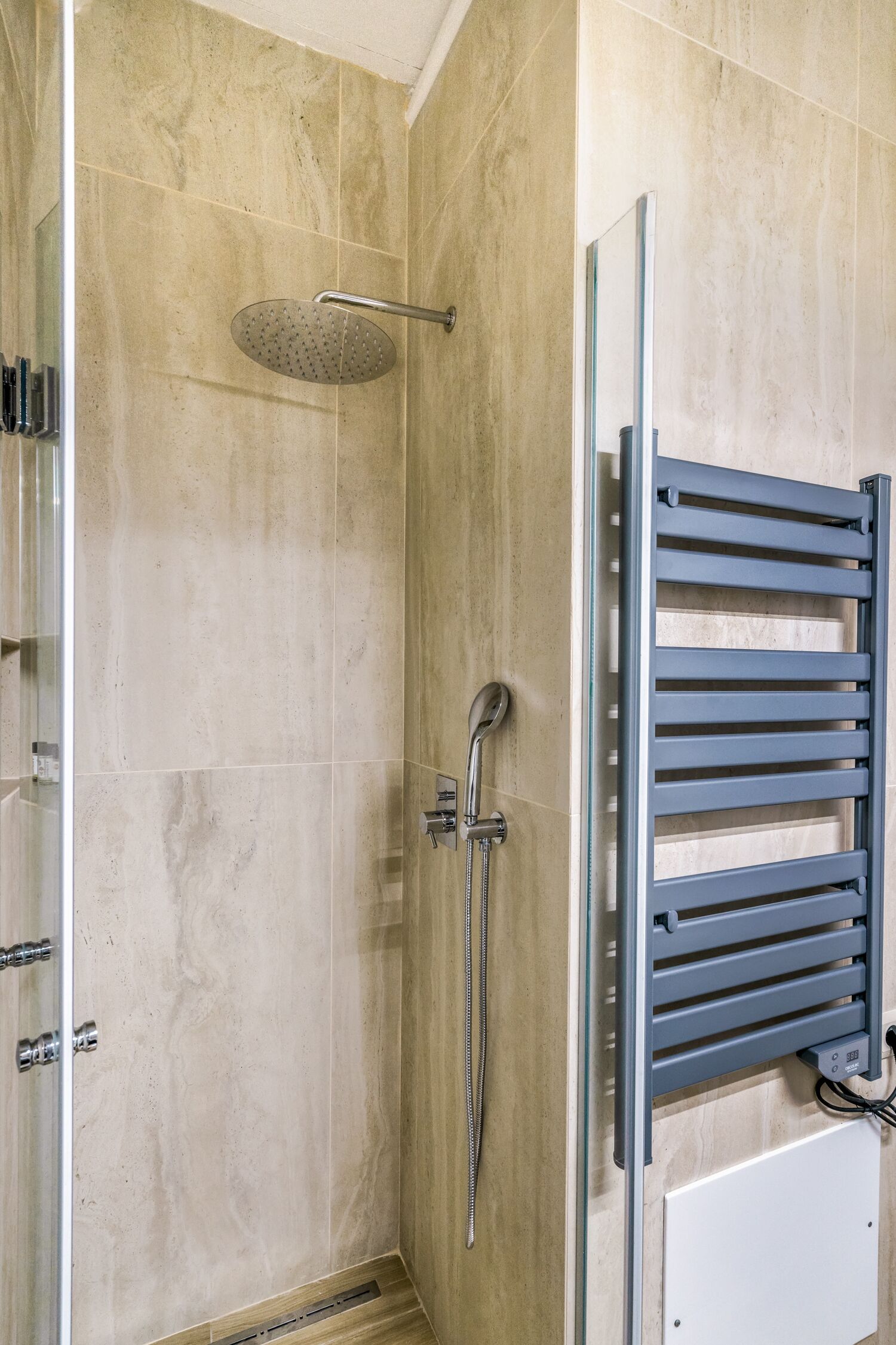 Eine Dusche mit Regendusche, Handbrause und Handtuchhalter.