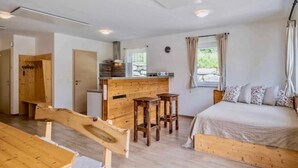 Una habitación con un banco de madera, una cama, una pequeña cocina y una ventana con cortinas.