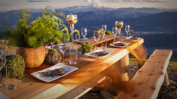 Une table de salle à manger en bois, mise avec des assiettes, des verres et un saladier, donnant sur un paysage montagneux.