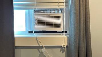A window with blinds, a white air conditioning unit labeled 'VISSANI,' and a curtain partially drawn to the side.