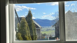 A window with a view of a house, a tree, and mountains in the background. - Valley Studio Private Suite (Abbotsford)