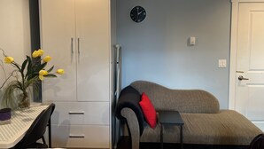 A room with a bed, a desk, a wardrobe, a clock, and a vase with flowers. - Valley Studio Private Suite (Abbotsford)