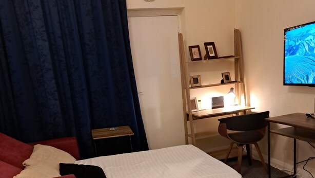 Ein Hotelzimmer mit zwei Betten, einem Schreibtisch mit Computer, einem Sessel und einem Fernseher.