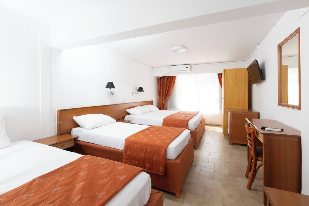 A hotel room with three beds, a desk, a chair, a TV, and a mirror.
