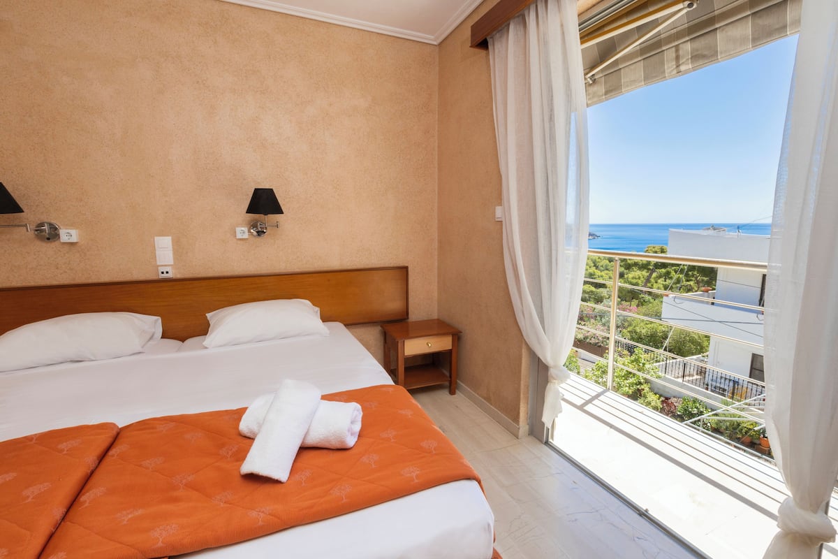 A hotel room with two beds, a nightstand, and a view of the sea.