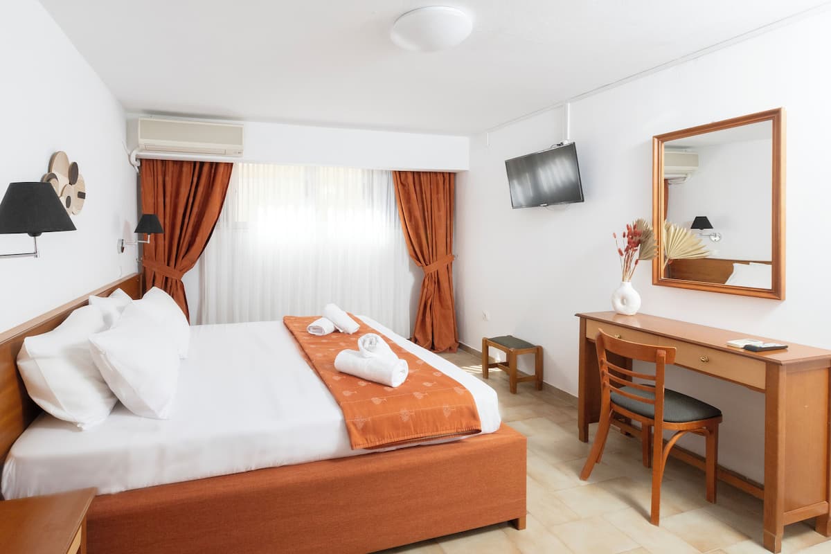 A hotel room with a bed, a desk, a chair, a TV, and a mirror.