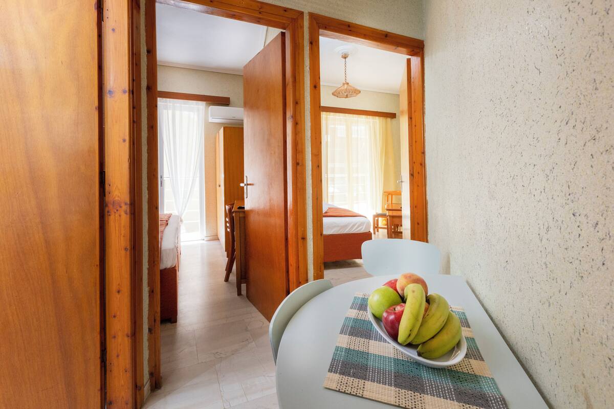 A hotel room with a bed, a table with a fruit bowl, and wooden doors leading to another room.