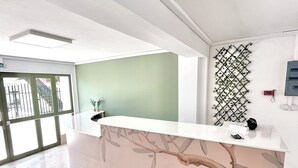 A reception desk with a modern design, a green accent wall, and a decorative plant wall. - Oelia Rooms & Apartments  (Aegina)