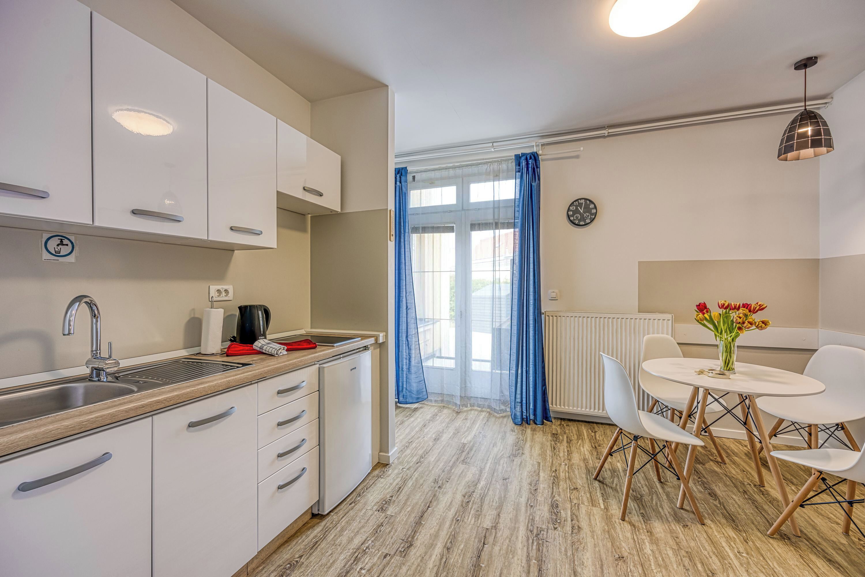A modern kitchen with white cabinets, a sink, and a dining area with a table and chairs.
