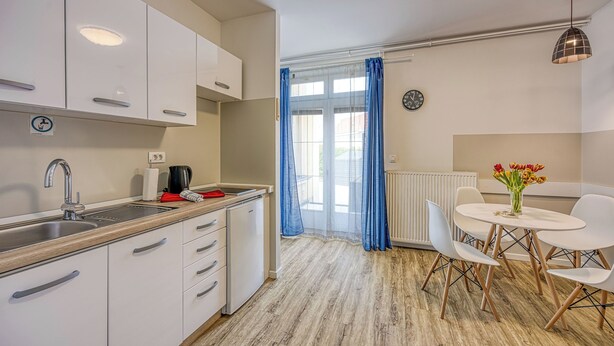 Une cuisine moderne avec des meubles blancs, un évier et un coin repas comprenant une table et des chaises.