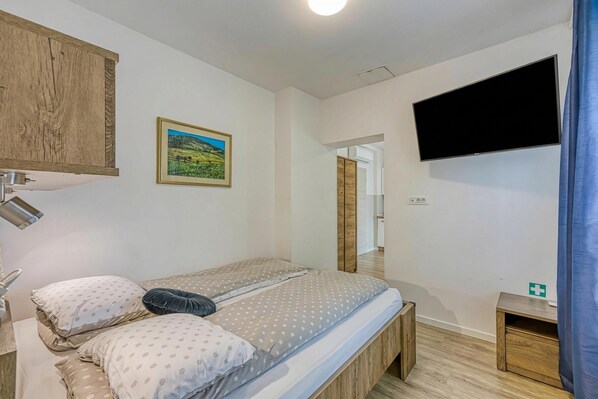 Un dormitorio con una cama, televisor montado, un aparador de madera, un cuadro enmarcado y una mesita de noche.