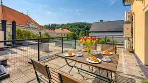 Ein Balkon mit Frühstückstisch, einer Bank und Blick auf Häuser und Bäume.