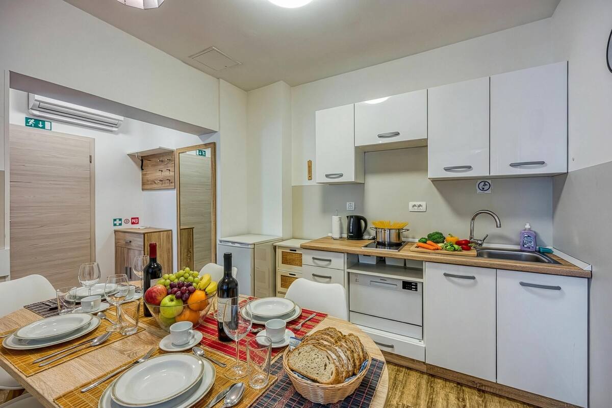 Una cocina moderna con armarios blancos, un fregadero y un comedor con una mesa para dos.