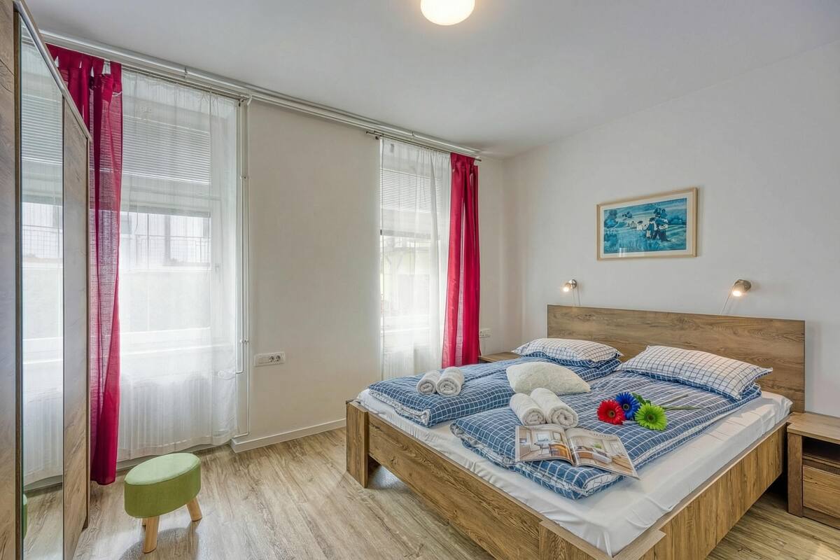 Un dormitorio con una cama de madera, un taburete verde y un cuadro en la pared.