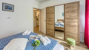 Ein Hotelzimmer mit Bett, einem Holzschrank, einem kleinen Hocker und Blick auf eine Küche.