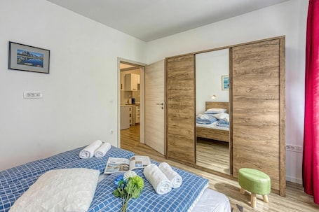 A hotel room with a bed, a wooden wardrobe, a small stool, and a view of a kitchen.. Jantar Apartments