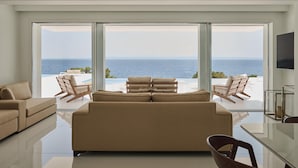 A modern living room with a large sofa, two armchairs, and a glass coffee table. A flat-screen TV is mounted on the wall. - OLYN VILLAS (Nikiti)