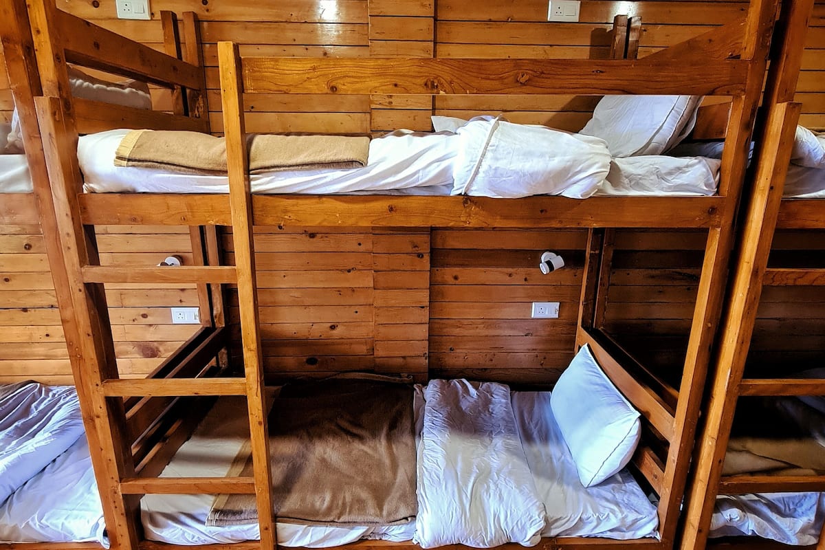 A bunk bed room with wooden walls and floors, equipped with a ladder and a small shelf.