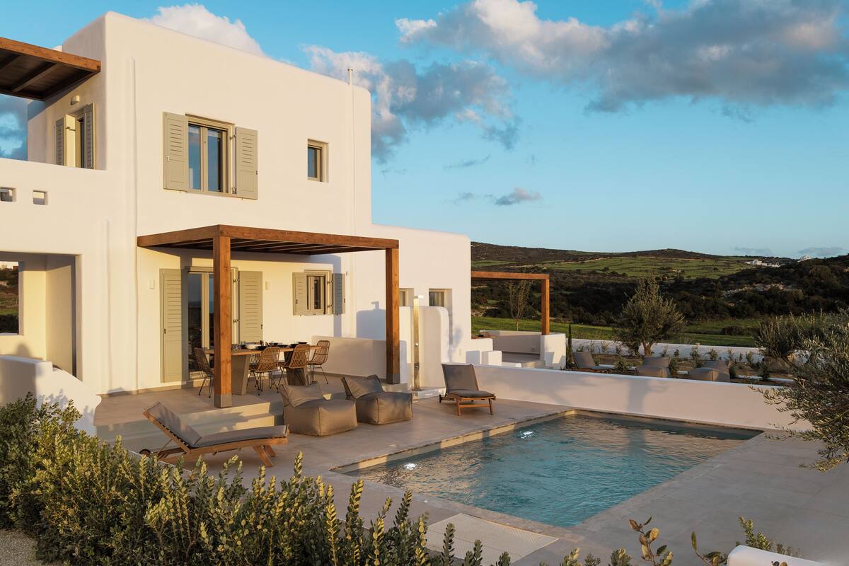 A modern two-story house with a pool, outdoor seating, and a view of the countryside.