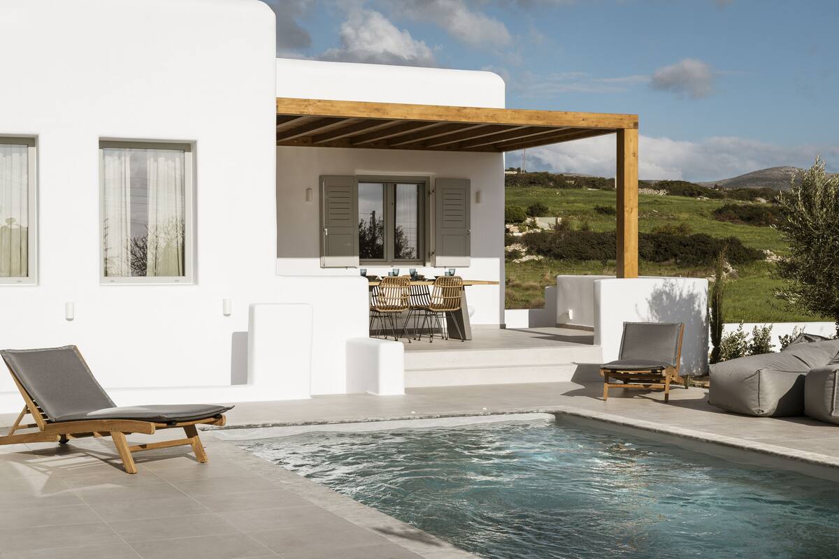 A modern outdoor pool area with a wooden pergola, lounge chairs, and a dining setup.