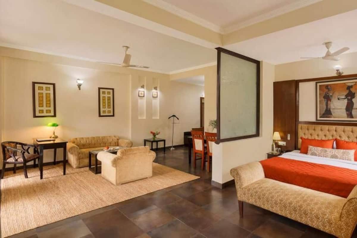 Une chambre d’hôtel avec un lit, deux canapés, un bureau, une chaise, une télévision et un tableau au mur.